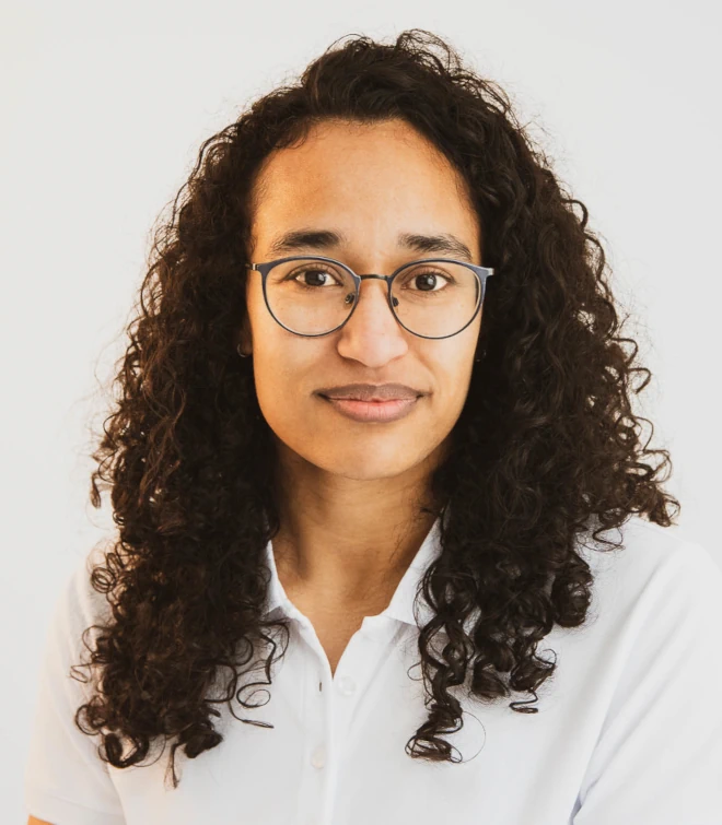 A Chiropractor in Berlin: Aimee in her mid-thirtys with long curly hair, wearing glasses and white polo shirt. Seriously-Friendly smiling - which was hard work to achieve.